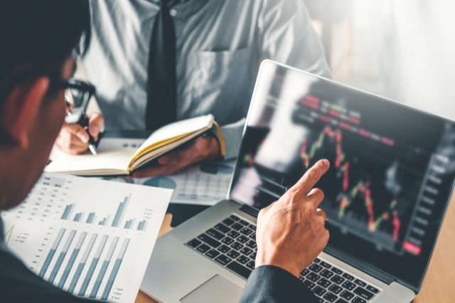 Two people reviewing market charts on a laptop
